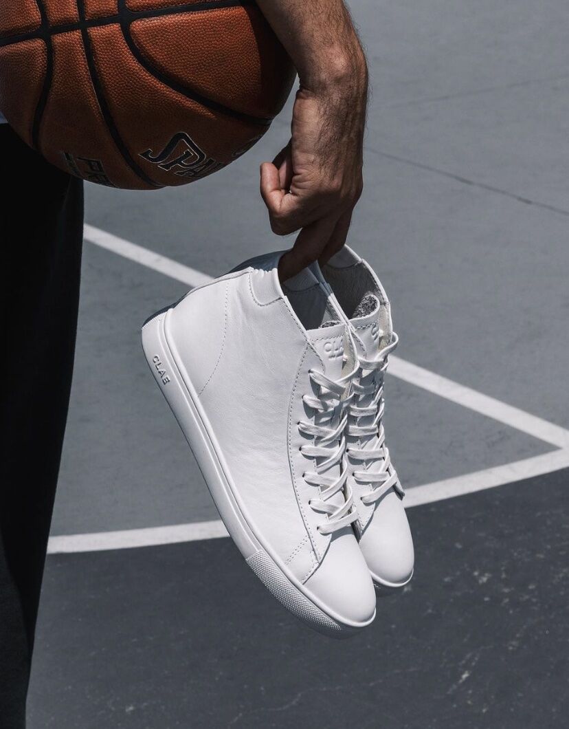 Person holding white hightop shoes and a basketball under arm