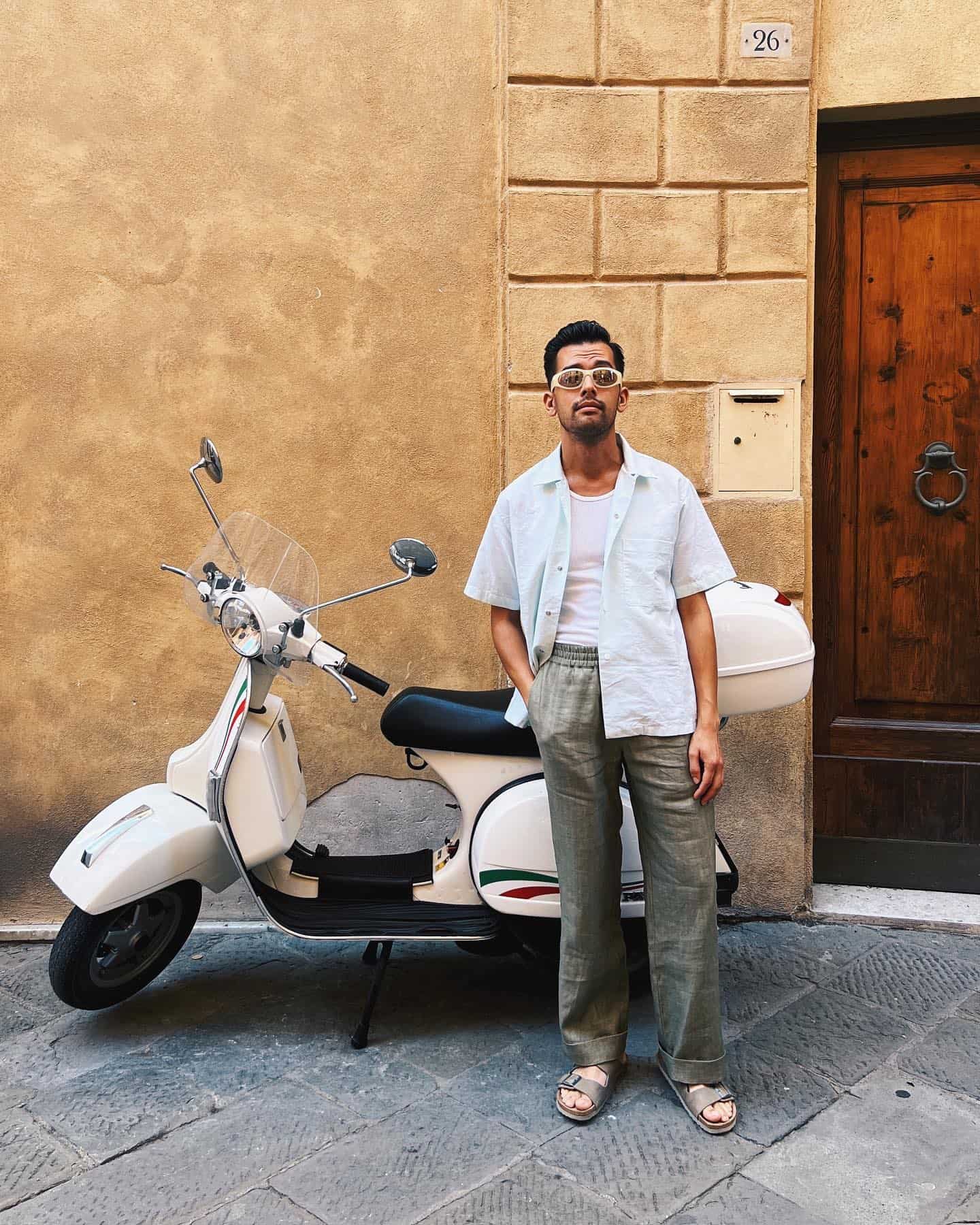 man in a linen outfit standing in front of a classic scooter