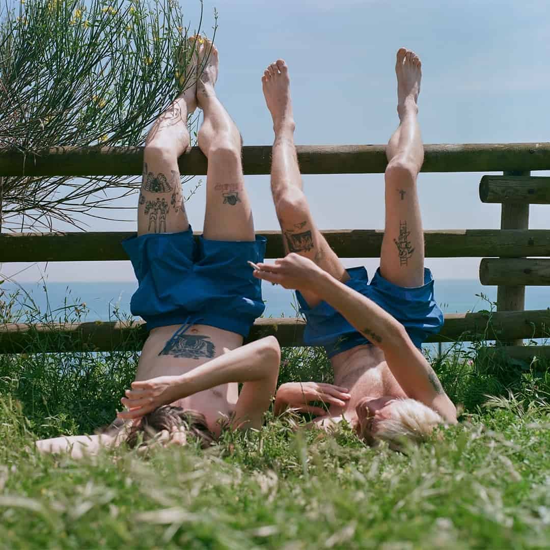 two men lying on the ground with feet resting on fence