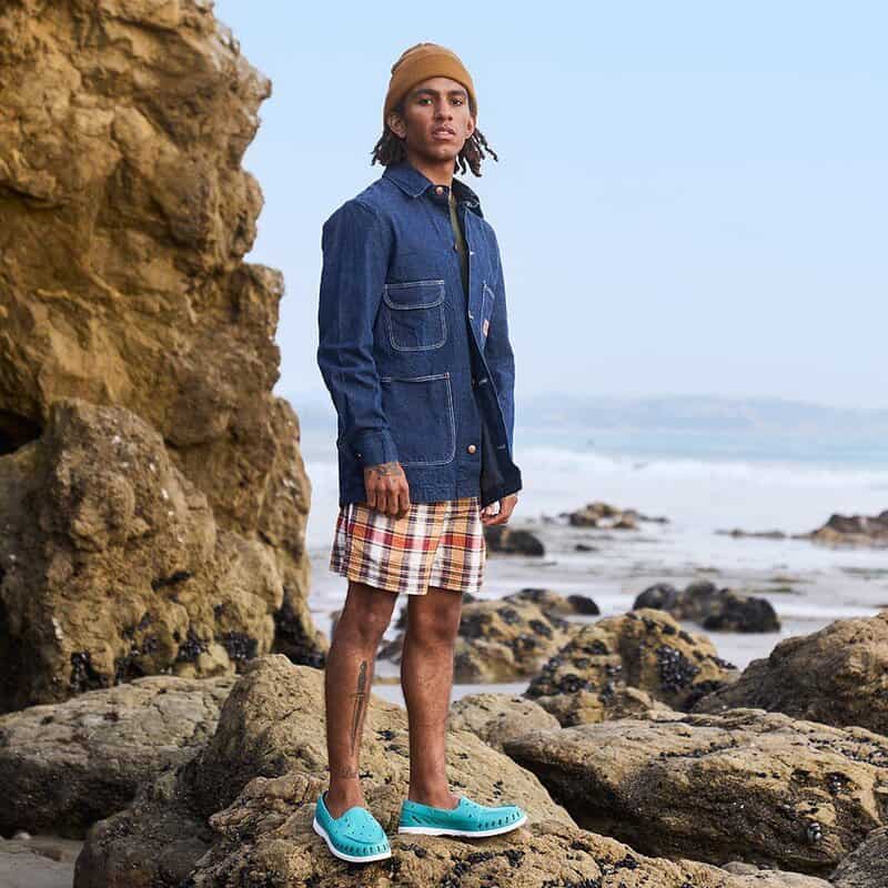 man standing on a rock at a beach wearing the sperry float boat shoes