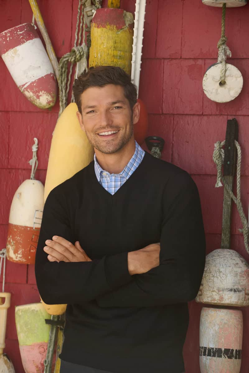 man wearing a black v-neck sweater over a blue checked shirt