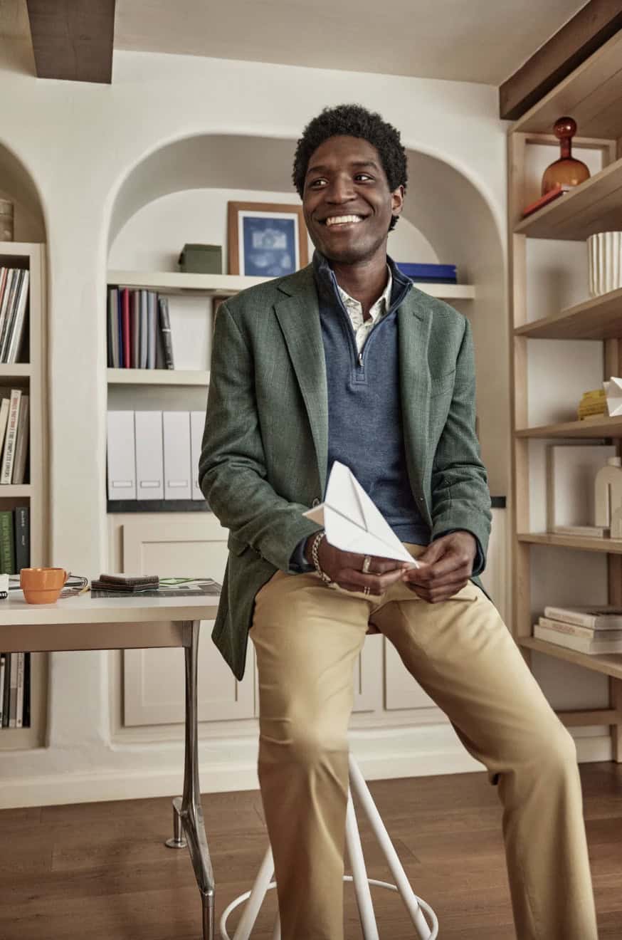 Man holding a paper airplane, leaning on a desk wearing men's wearhouse clothing