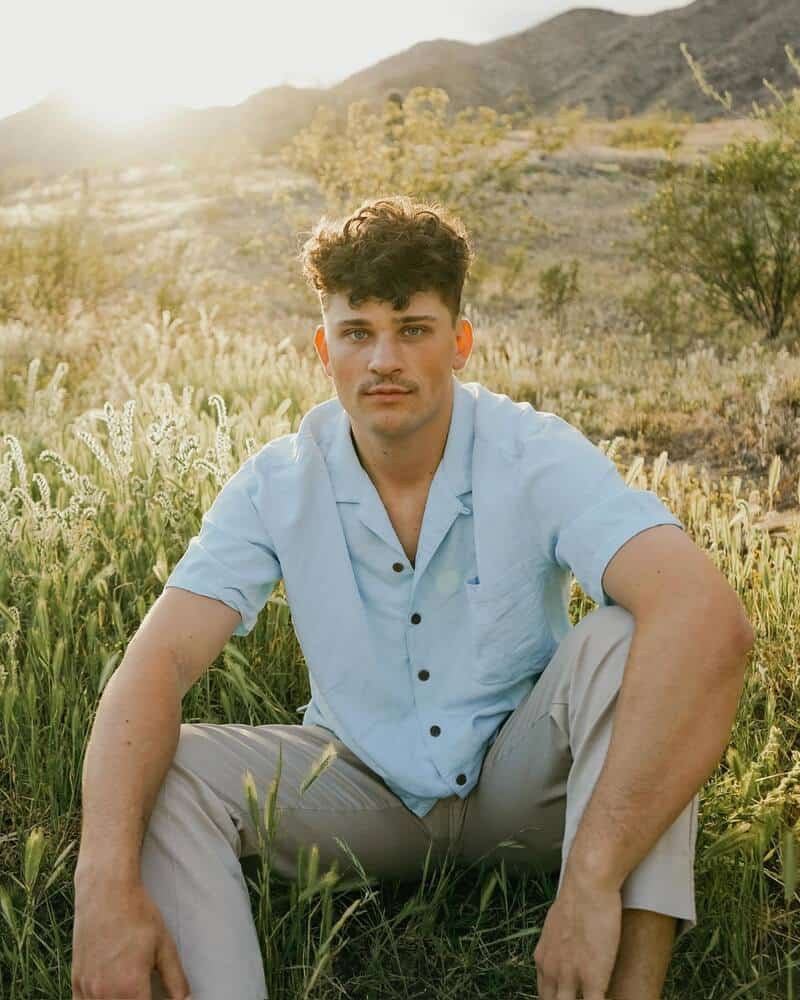 man with blue eyes sitting on a field