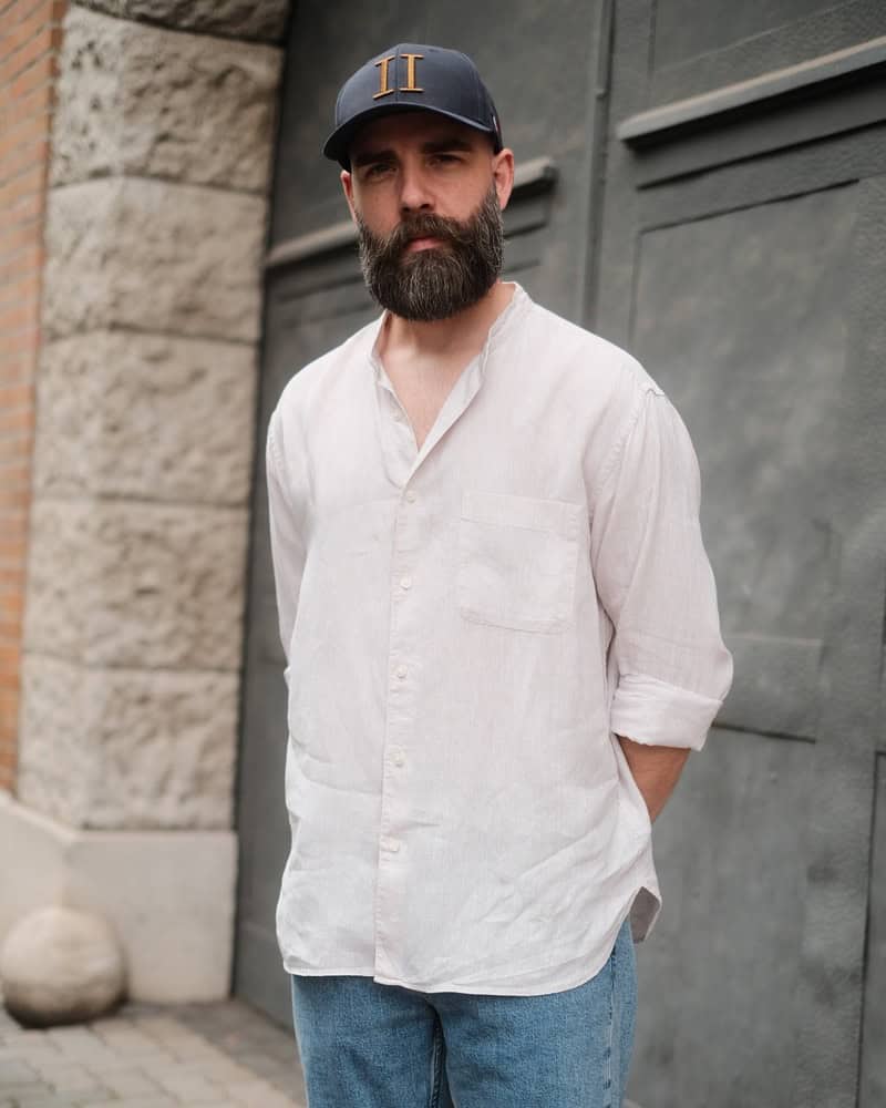 man with a full beard wearing a white shirt and a blue hat