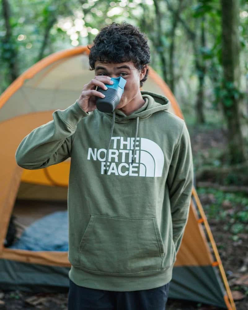 man drinking in a cup infront of a tent wearing the north face hoodie