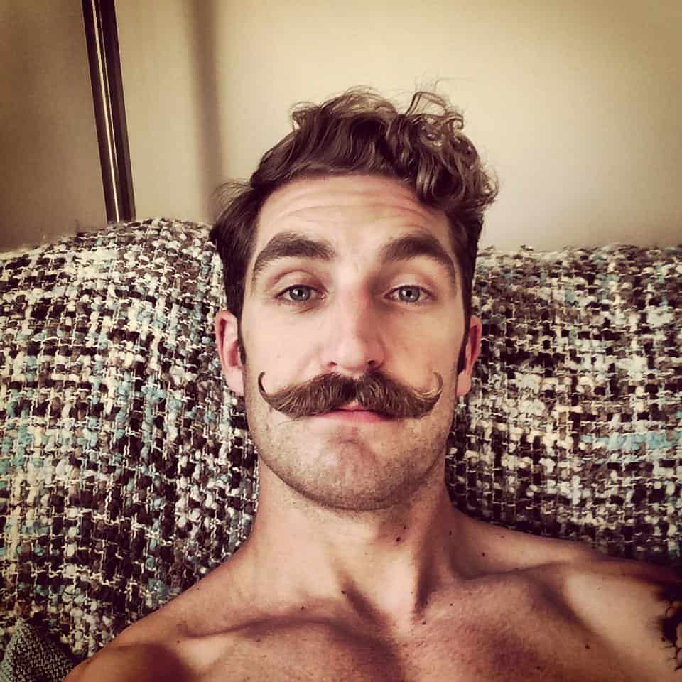 man with a handlebar mustache style sitting on a couch